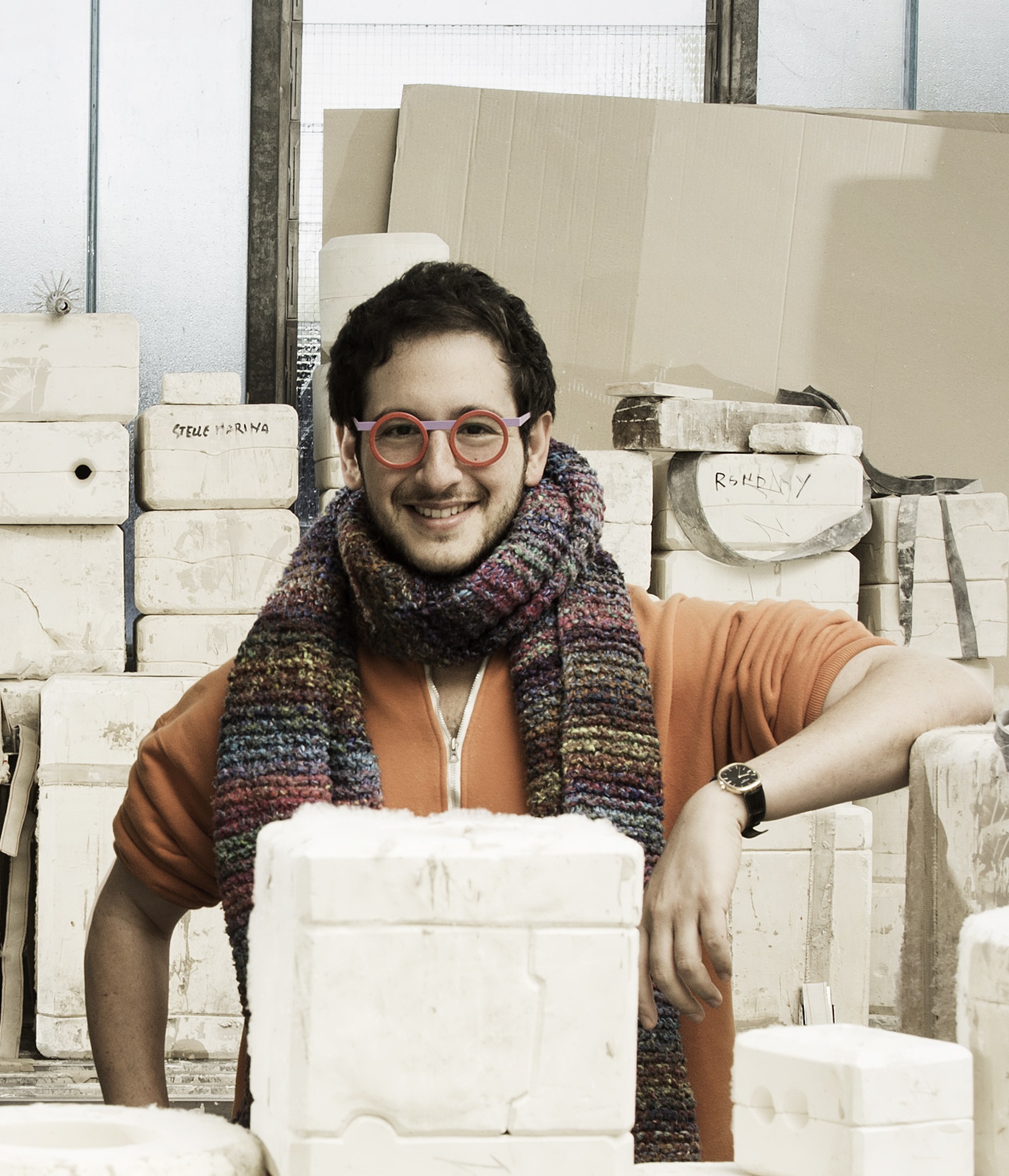 A photo showing the artist Adam Nathaniel Furman behind and in front of grey architectural forms. Photo by Laila Pozzo